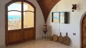 A spacious room with a tiled floor, a large arched window, a flat-screen TV mounted on the wall, and a rustic wooden door. - Tala boutique accommodation 15 (Hurghada)