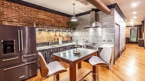 Cocina moderna con pared de ladrillo, electrodomésticos de acero inoxidable y comedor con mesa y sillas de madera.