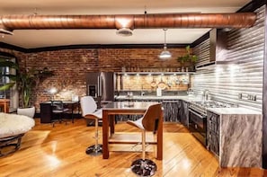 A modern kitchen with a brick wall, stainless steel appliances, and wooden flooring. - Luxury Downtown Paducah 2 Bedroom 2 Bath Double Condo (Paducah)