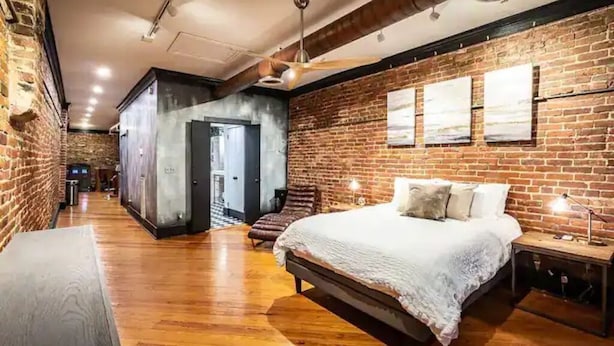 Un dormitorio con una cama grande, suelo de madera, paredes de ladrillo y un ventilador de techo.