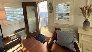 Una habitación acogedora con suelo de madera, un sofá de cuero marrón, una mesita de madera, un aparador blanco y un ventanal con persianas.