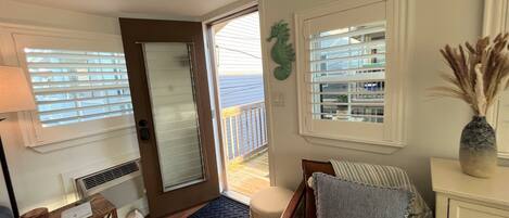 A cozy room with a wooden floor, a brown leather sofa, a small wooden side table, a white dresser, and a large window with blinds.