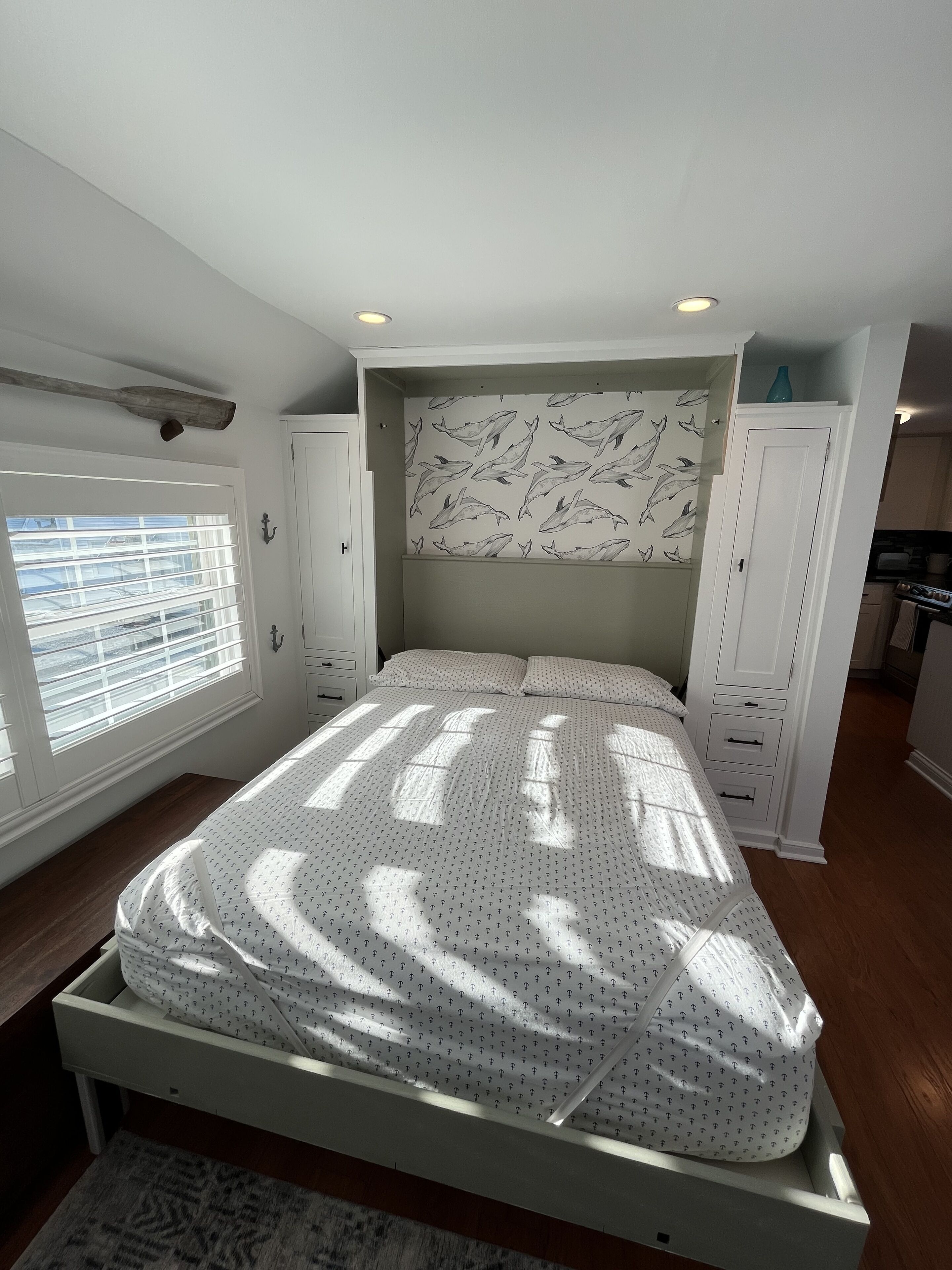 Une chambre avec un lit, une fenêtre avec des stores, une armoire et, au fond, un coin cuisine.