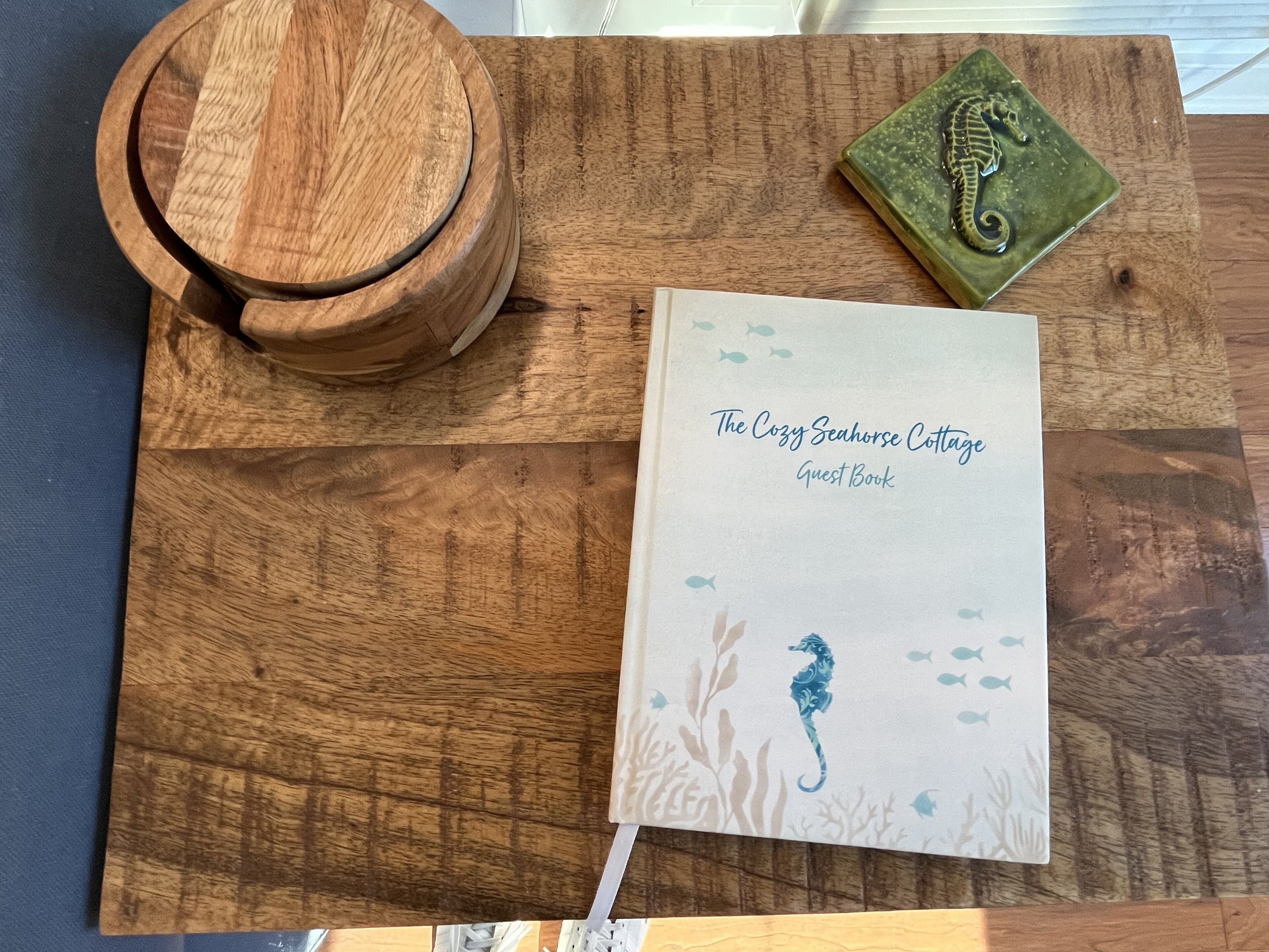 A wooden table with a book titled "The Cozy Seahorse Cottage Guest Book" and a decorative plate with a seahorse.