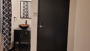 Un baño con un mueble negro, un espejo grande, una puerta negra y una cortina estampada.