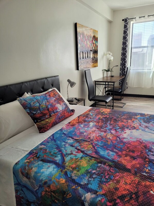 A bedroom with a bed, a desk, a chair, and a window with curtains.