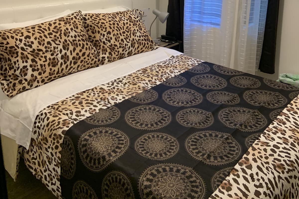 Une chambre à coucher avec un lit, une table de chevet, une lampe et une fenêtre avec des rideaux.