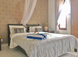 Cozy retreat with a large bed, white lace bedspread, and striped blanket, flanked by two pillows and a nightstand with a lamp.