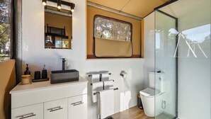 Ein modernes Badezimmer mit einem weißen Waschtisch, einem Spiegel, einem Fenster und einer Glasdusche.