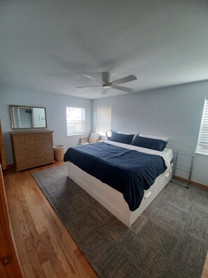 Un dormitorio con cama, cómoda, ventilador de techo y ventanas.