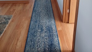 A hallway with a blue patterned carpet, wooden flooring, and a white air conditioning unit on the left.