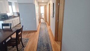 A hallway with a wooden floor, a dining area with a table and chairs, and a kitchen area with cabinets and appliances.