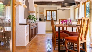 Un coin repas avec une table et des chaises en bois, un luminaire suspendu et une cuisine en arrière-plan.
