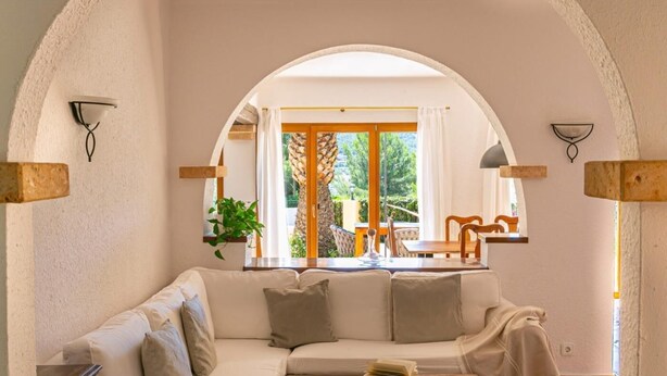 Un salon chaleureux avec un canapé blanc, une table basse et, à travers une porte en arc, une vue sur la salle à manger.