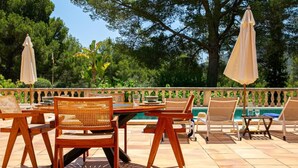Une terrasse extérieure avec des tables et des chaises en bois, une piscine et des parasols.