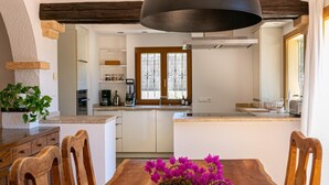 Une cuisine moderne avec un îlot central, des chaises en bois et une table à manger agrémentée d’un panier tressé rempli de fleurs.