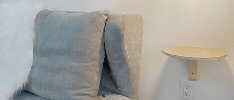 A room with a grey sofa, a wall-mounted light, and a small wooden shelf.