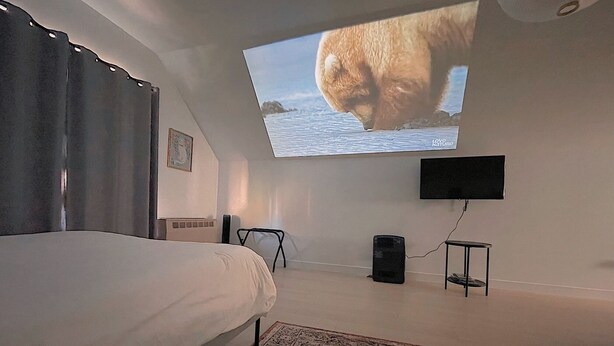 Ett sovrum med en säng, en tv som är monterad på väggen, ett litet bord och en matta.