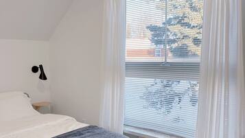 A bedroom with a bed, a bedside table, a lamp, and a window with blinds and curtains.