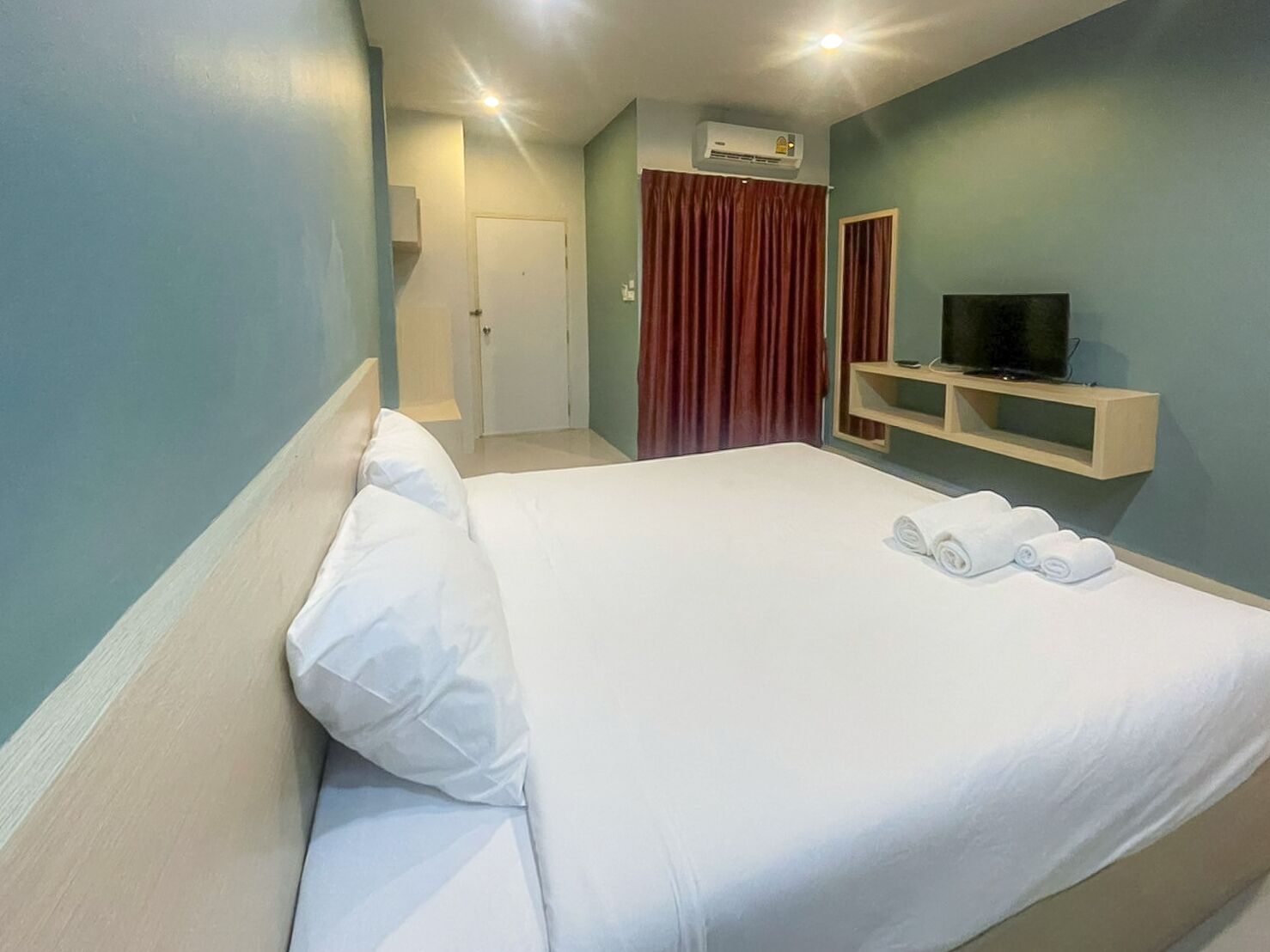 A hotel room with a bed, a TV, and a shelf with towels.