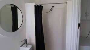A bathroom with a white sink, a round mirror, a black shower curtain, and a door leading to another room. - Cedric Cottage, 1B Cedric Court (Mallacoota)