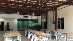 A large indoor space with multiple tables and chairs, a green partition, and a sign reading "Cafeteria". - Badul Homestay (Kuching)