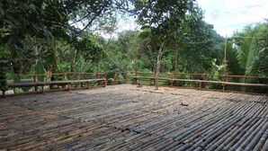 A bamboo deck with a rustic wooden fence, surrounded by dense tropical foliage. - Badul Homestay (Kuching)