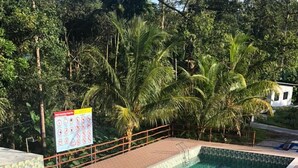 A swimming pool with a tiled deck, surrounded by palm trees and a signboard. - Badul Homestay (Kuching)
