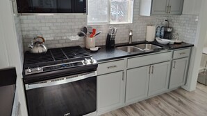 A modern kitchen with white cabinets, a black stove, a built-in oven, a stainless steel sink, and a window with a floral curtain.