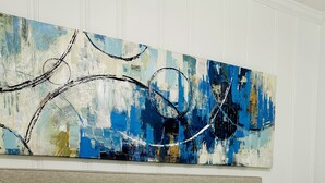 A bed with white bedding and striped pillows, a headboard, and a large abstract painting above.