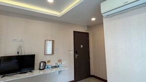 A hotel room with a flat-screen TV, a small shelf with toiletries, a door, and an air conditioning unit. - Amber Inn (Bangkok)