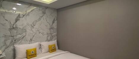 A modern hotel room with a marble wall, a neatly made bed with white linens, and a ceiling with recessed lighting.