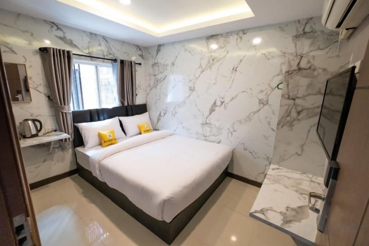 Un dormitorio moderno con una cama grande, paredes de mármol, un televisor y una pequeña mesa con una tetera.