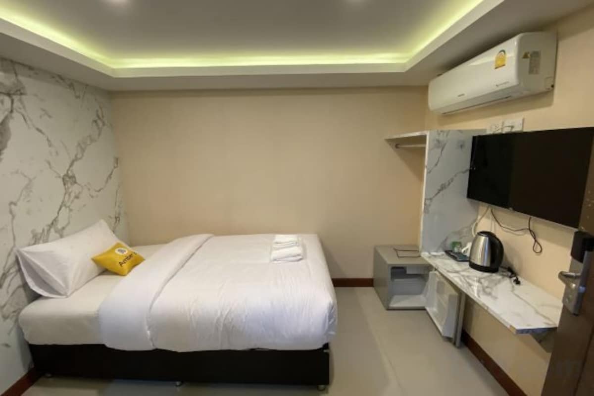 Habitación de hotel con cama, televisión, una kitchenette pequeña y pared con diseño de mármol.