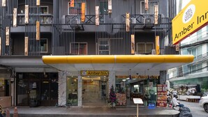 A multi-story building with a modern facade, featuring vertical wooden slats and a prominent yellow sign for 'Amber Inn'. - Amber Inn (Bangkok)