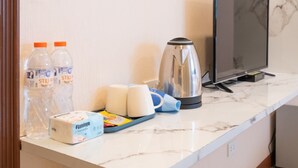A hotel room with a marble countertop, a wooden stool, a television, a kettle, and toiletries. - Amber Inn (Bangkok)