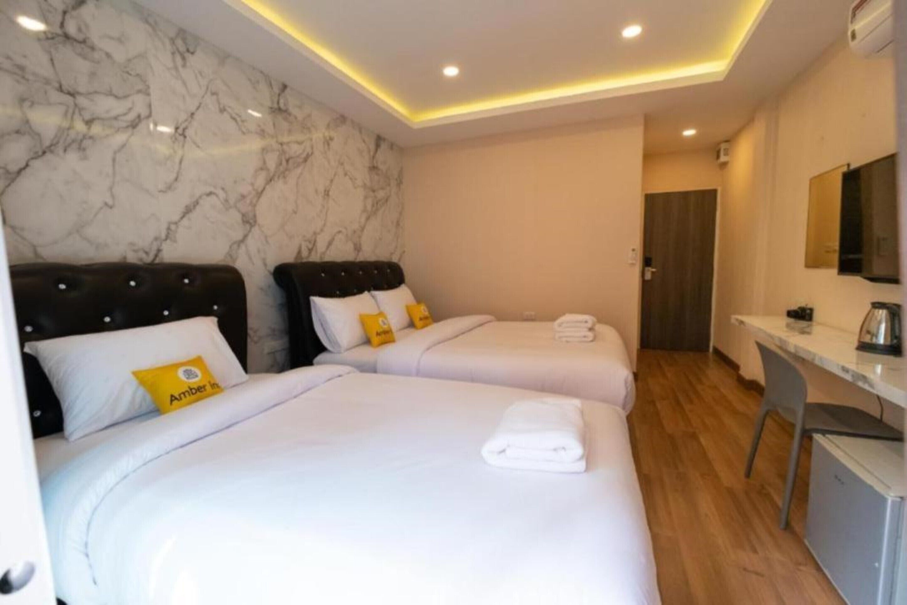 A hotel room with two beds, marble walls, a desk, and a mirror.