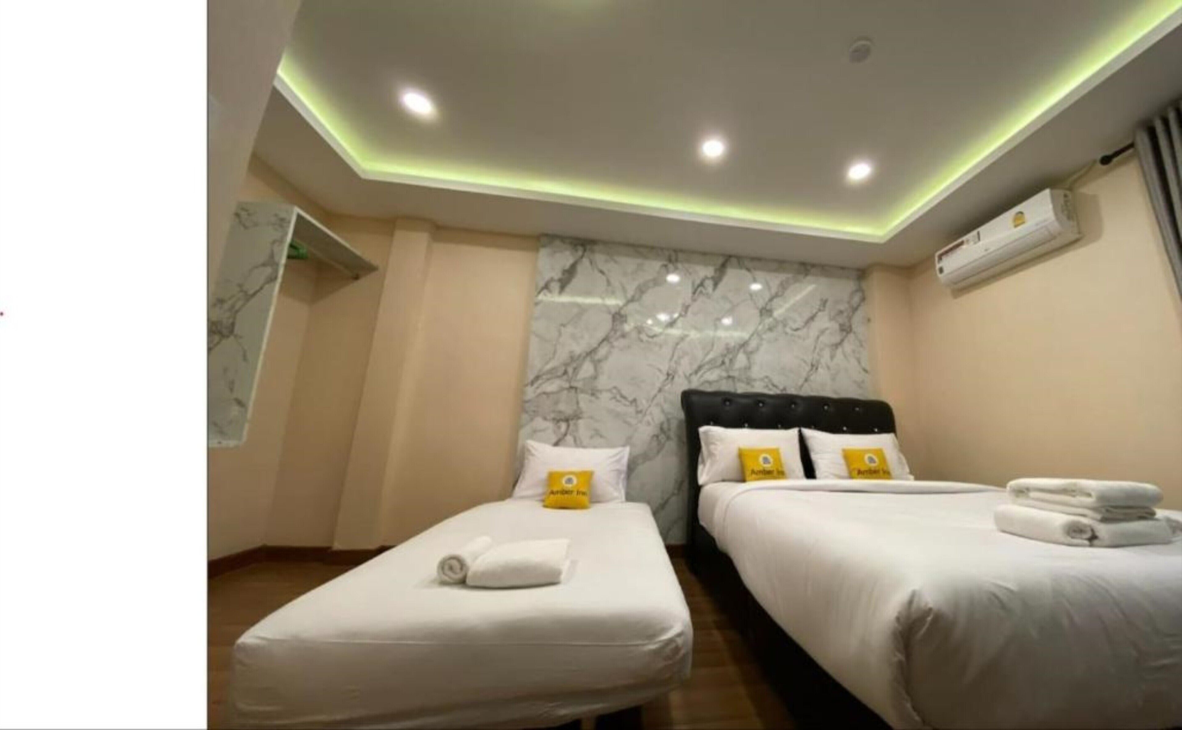 A hotel room with two beds, marble wall, ceiling lights, and an air conditioning unit.