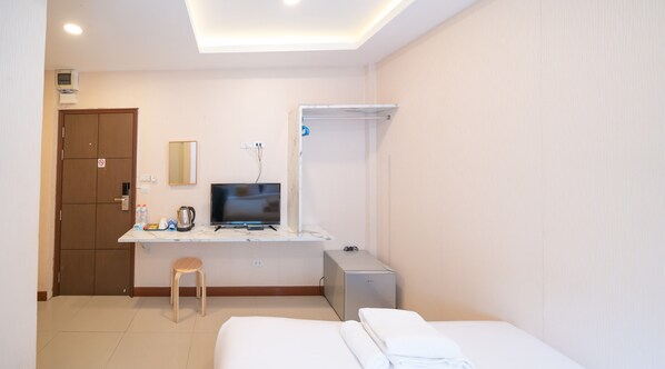 A hotel room with a bed, a desk with a TV, a small refrigerator, a mirror, and a door with a sign.