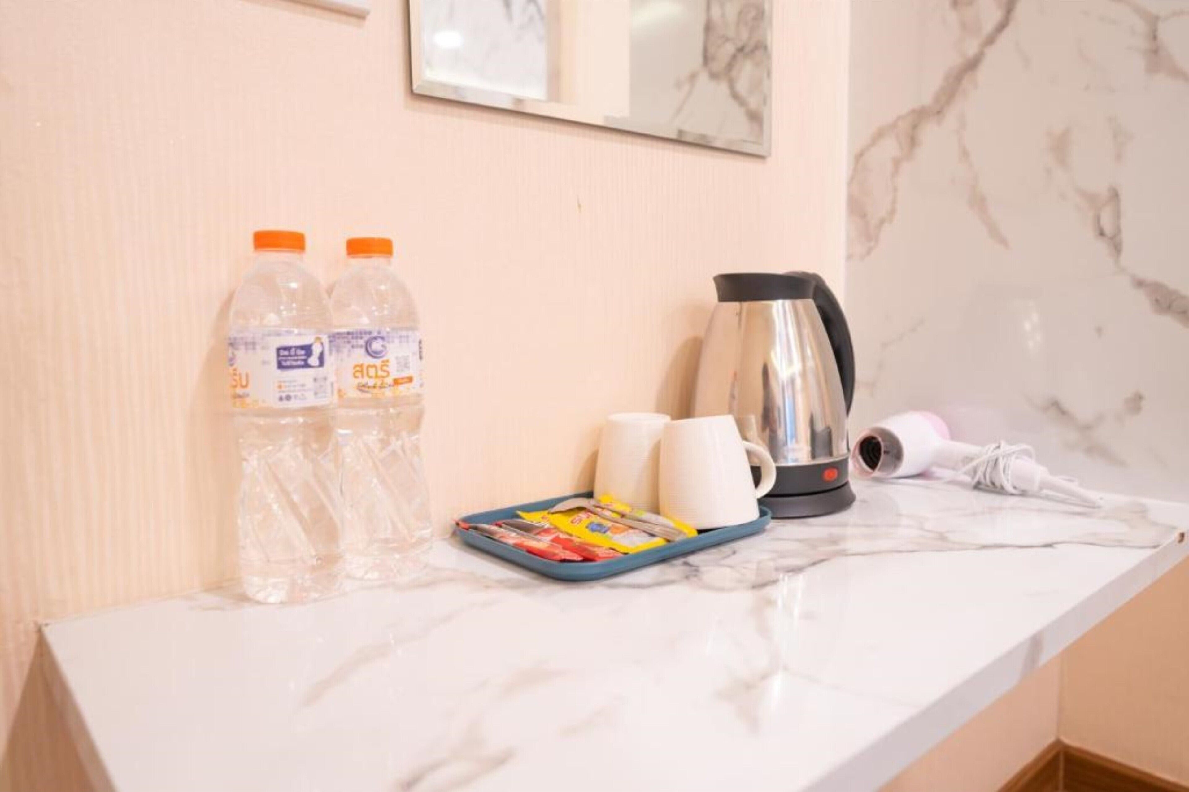 Un plan de travail en marbre avec deux bouteilles d’eau, un plateau avec des magazines, deux tasses blanches, une bouilloire électrique argentée et un sèche-cheveux.