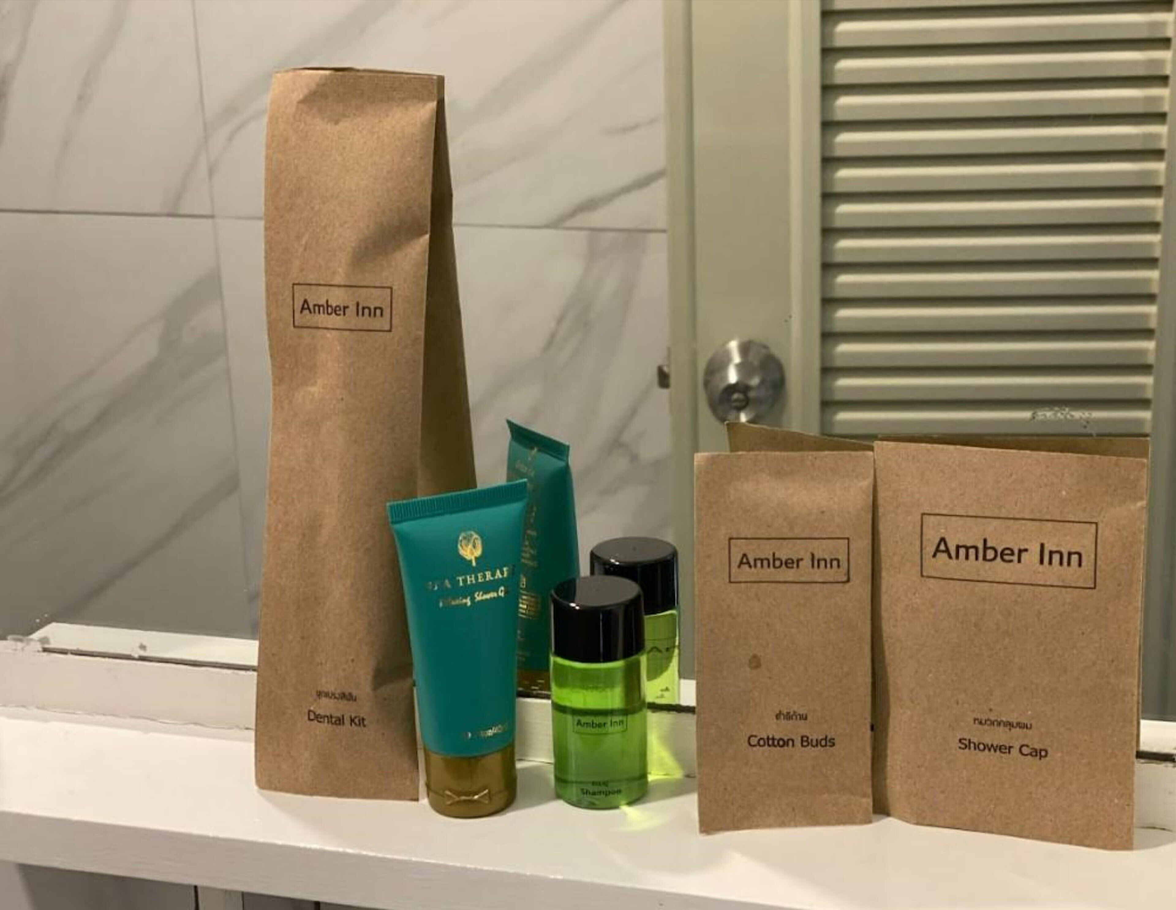 A bathroom shelf with various toiletries including a dental kit, cotton buds, and a shower cap, all labeled with 'Amber Inn'.