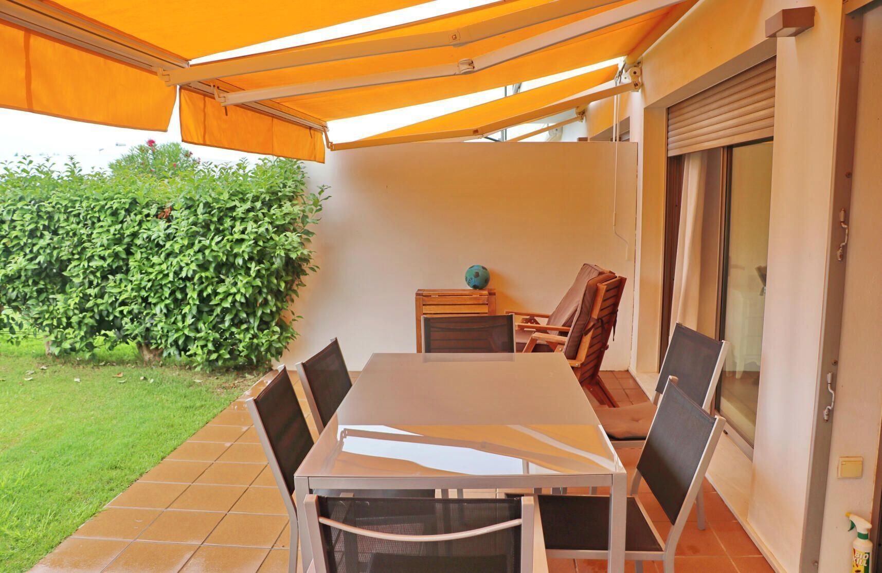 Un patio con mesa y sillas, un área cubierta y vistas a un jardín y un edificio.