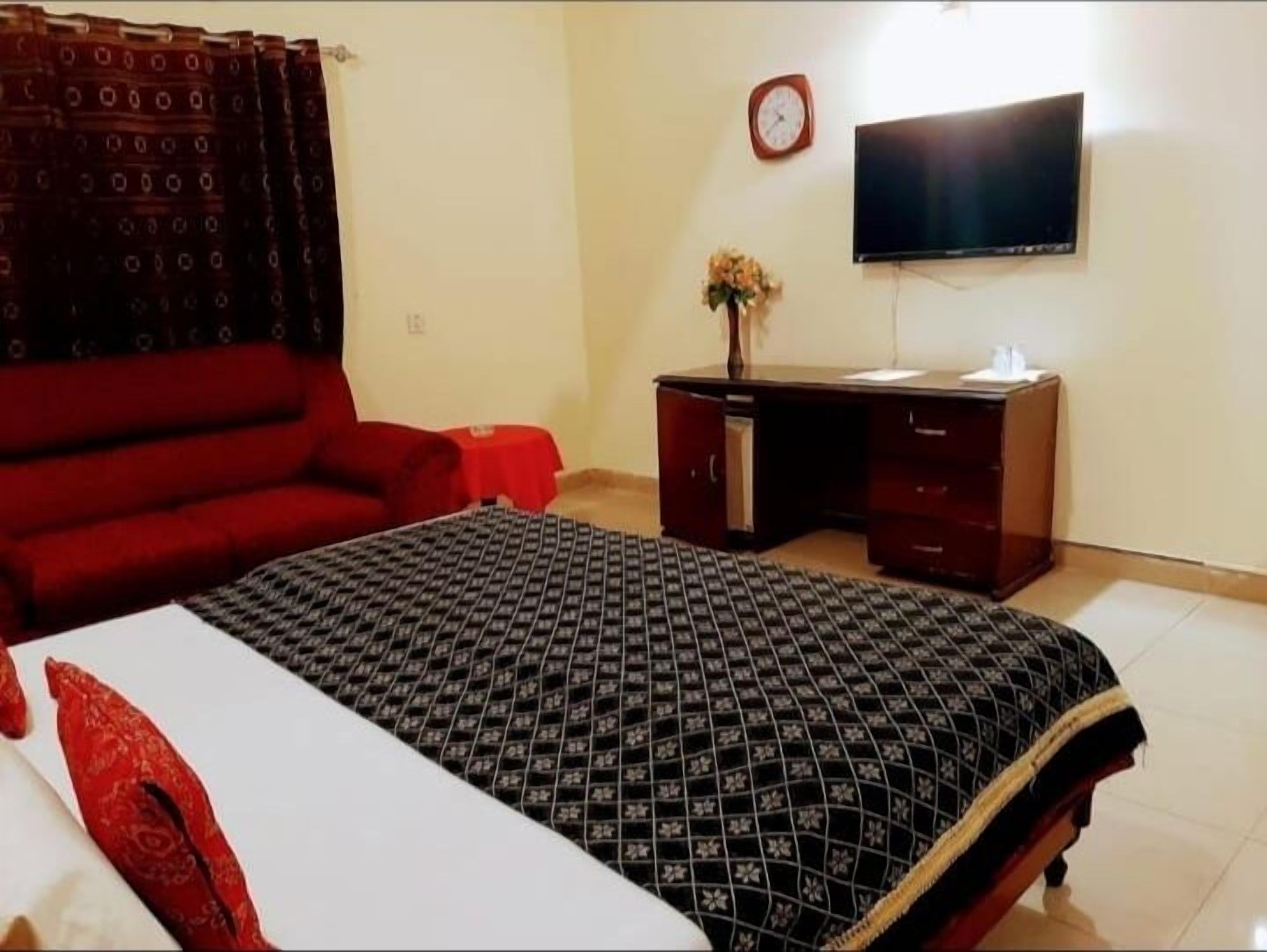 Una habitación de hotel con cama, escritorio, silla, televisor y un reloj en la pared.