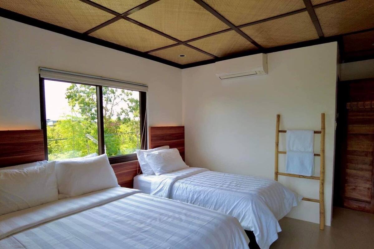 Habitación de hotel con dos camas, un ventanal grande y una escalera de madera.