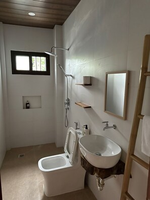 Een badkamer met toilet, wastafel, douche en een klein raam.