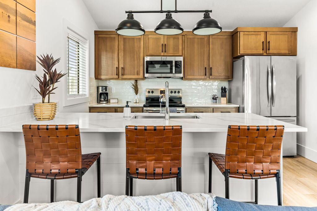 A modern kitchen with wooden cabinets, stainless steel appliances, and a central island with three woven chairs.