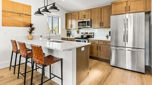 A modern kitchen with wooden cabinets, stainless steel appliances, and a central island with bar stools. - New Build, Great Value near Downtown Vancouver & Waterfront (Vancouver)