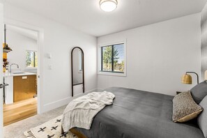 Ein Schlafzimmer mit Bett, einem Fenster mit Jalousien, einer Nachttischlampe und einer Tür zu einem Badezimmer.