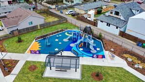 A playground with slides and climbing structures, surrounded by a fenced area with benches and a small garden. - New Build, Great Value near Downtown Vancouver & Waterfront (Vancouver)