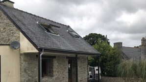 Ein Steinhaus mit geneigtem Dach, einer Laube und einer Zuwegung mit Kies.